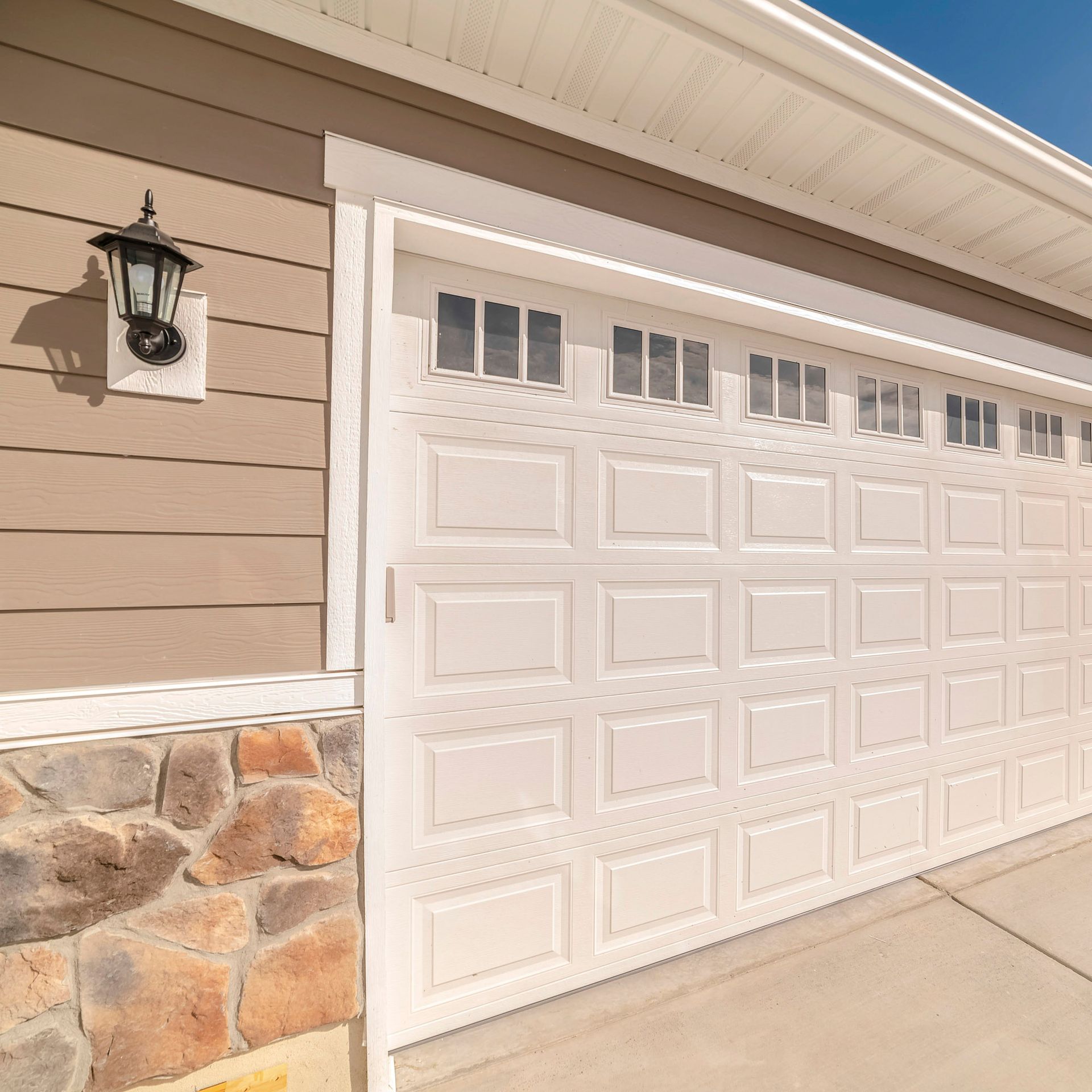 White double sectional garage door with raised panels, decorative top windows, and a lantern light.