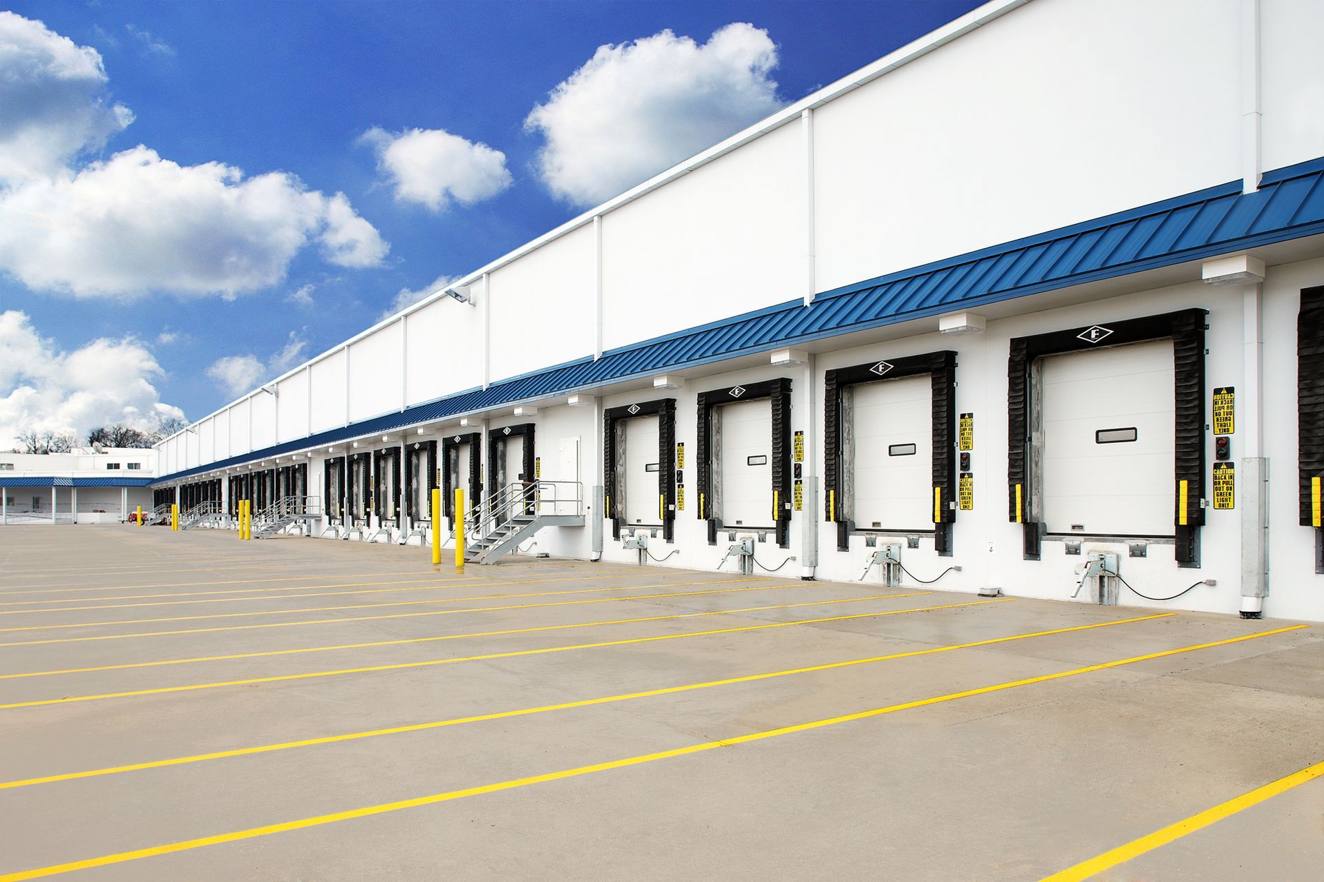 Rows of white commercial overhead garage doors along a warehouse loading dock under a blue sky