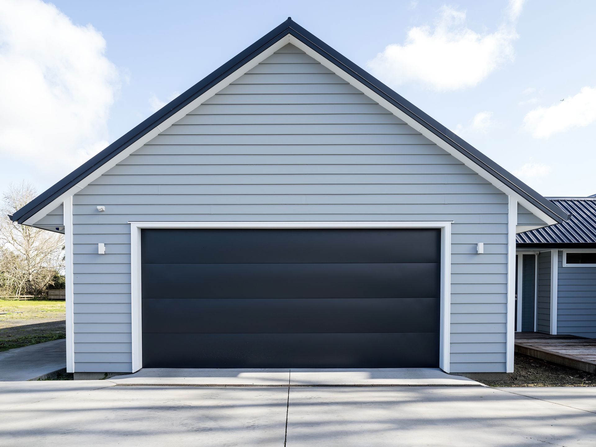 Gray house exterior with a large dark garage door and clean concrete driveway.