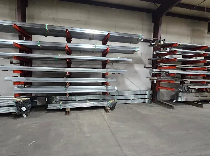 Warehouse storage racks holding long metal beams and red-tipped parts along a concrete floor.