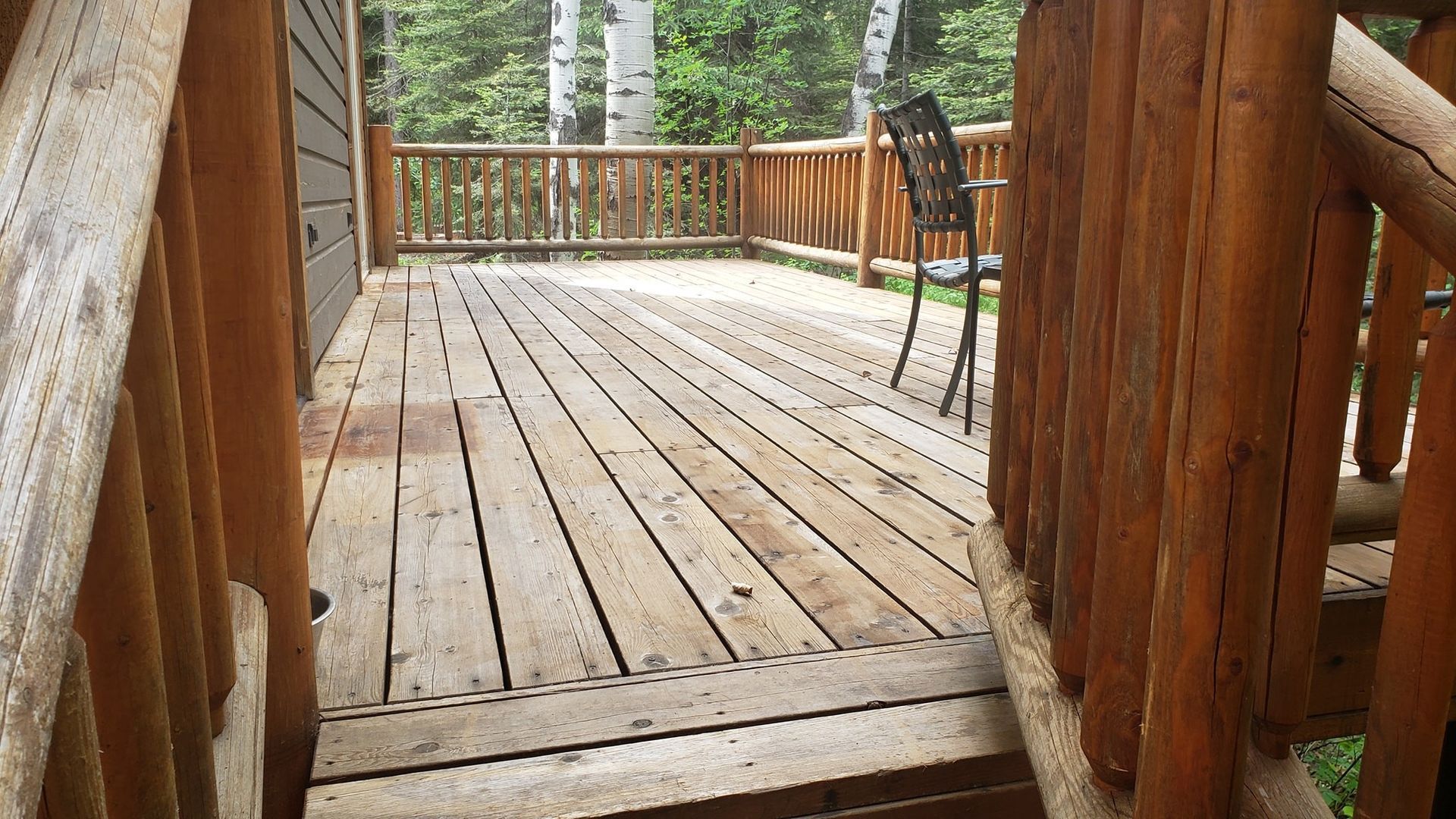 Wooden cabin deck with log railings and a chair, overlooking a forest.