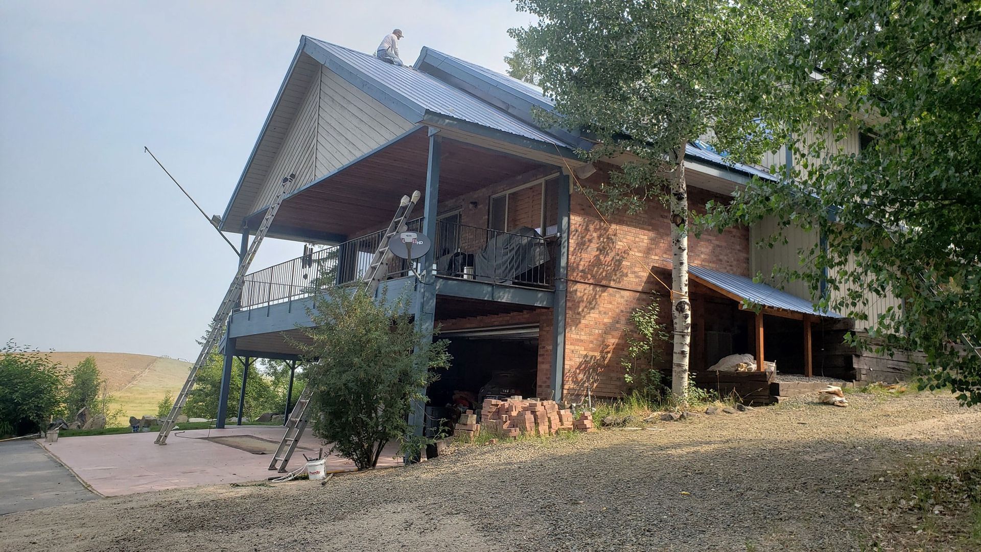 Two-story brick house with a covered porch on a grassy hillside, viewed from the front-left side.