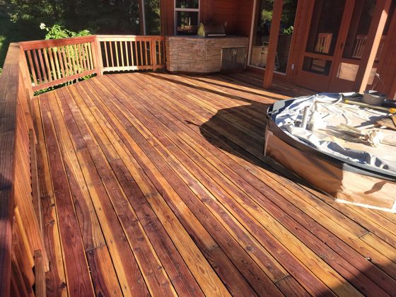 Wooden deck with sunlit railings and a covered hot tub beside brick house windows