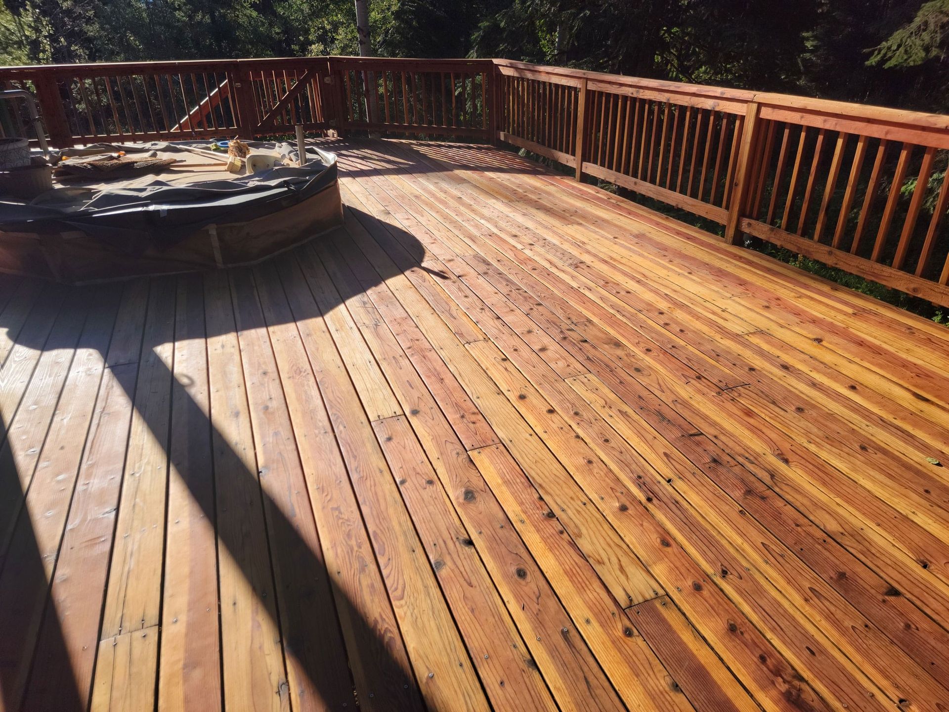 Wooden deck with a hot tub and railing, lit by sunlight and long shadows