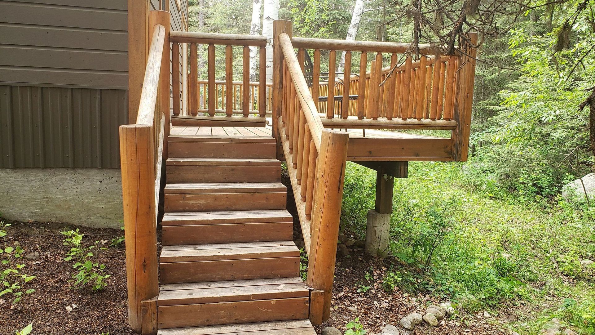 Wooden outdoor stairs leading to a raised deck beside a house, surrounded by greenery