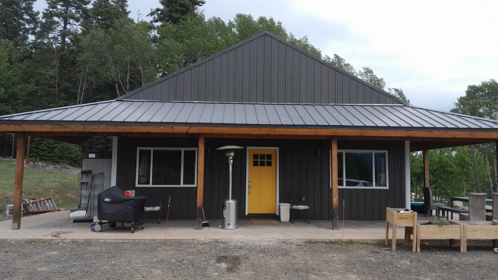 Rustic cabin with black roof, yellow door, and porch furniture surrounded by trees