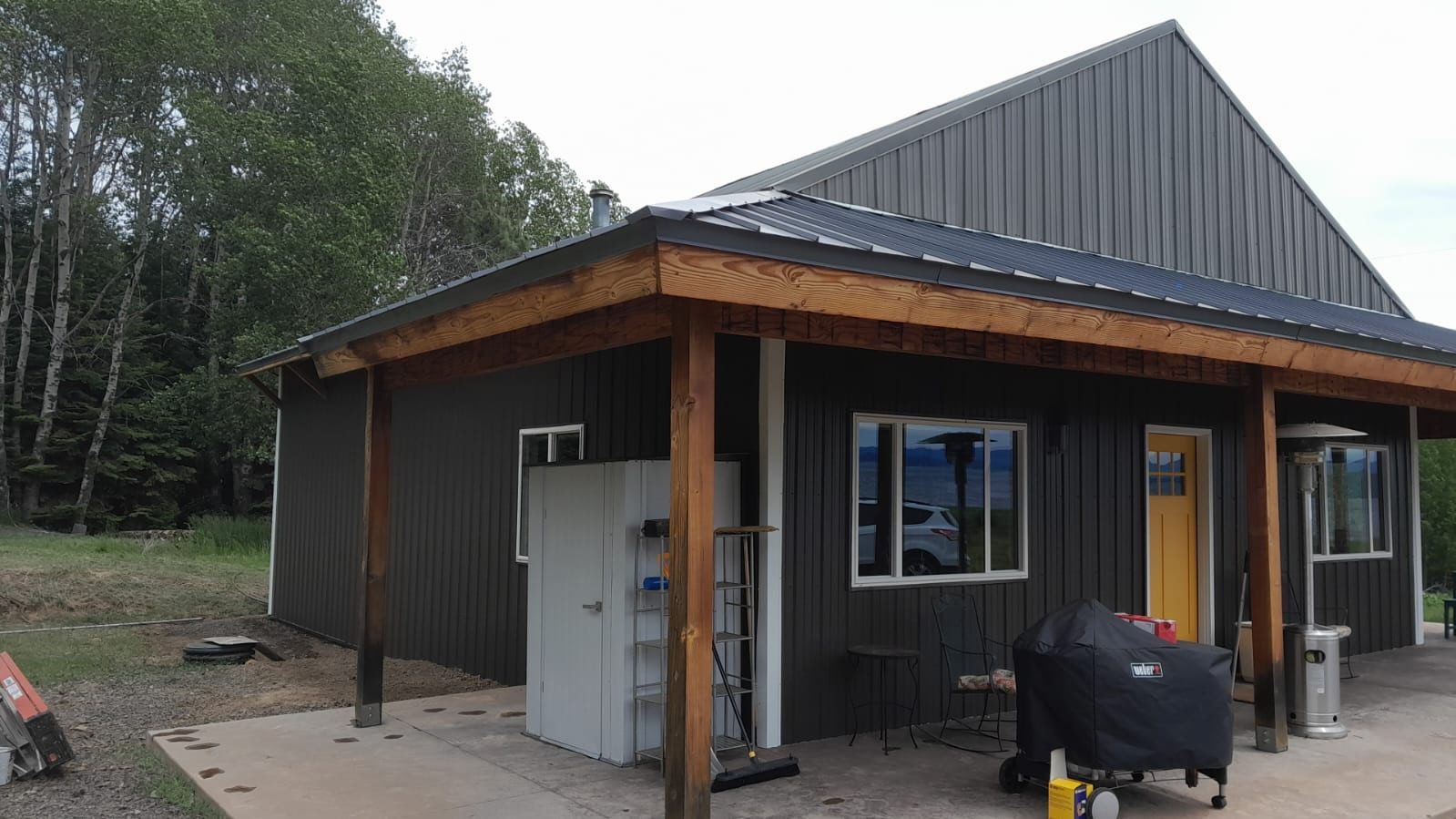 New house exterior with gray siding, wooden porch posts, and a black grill on the patio