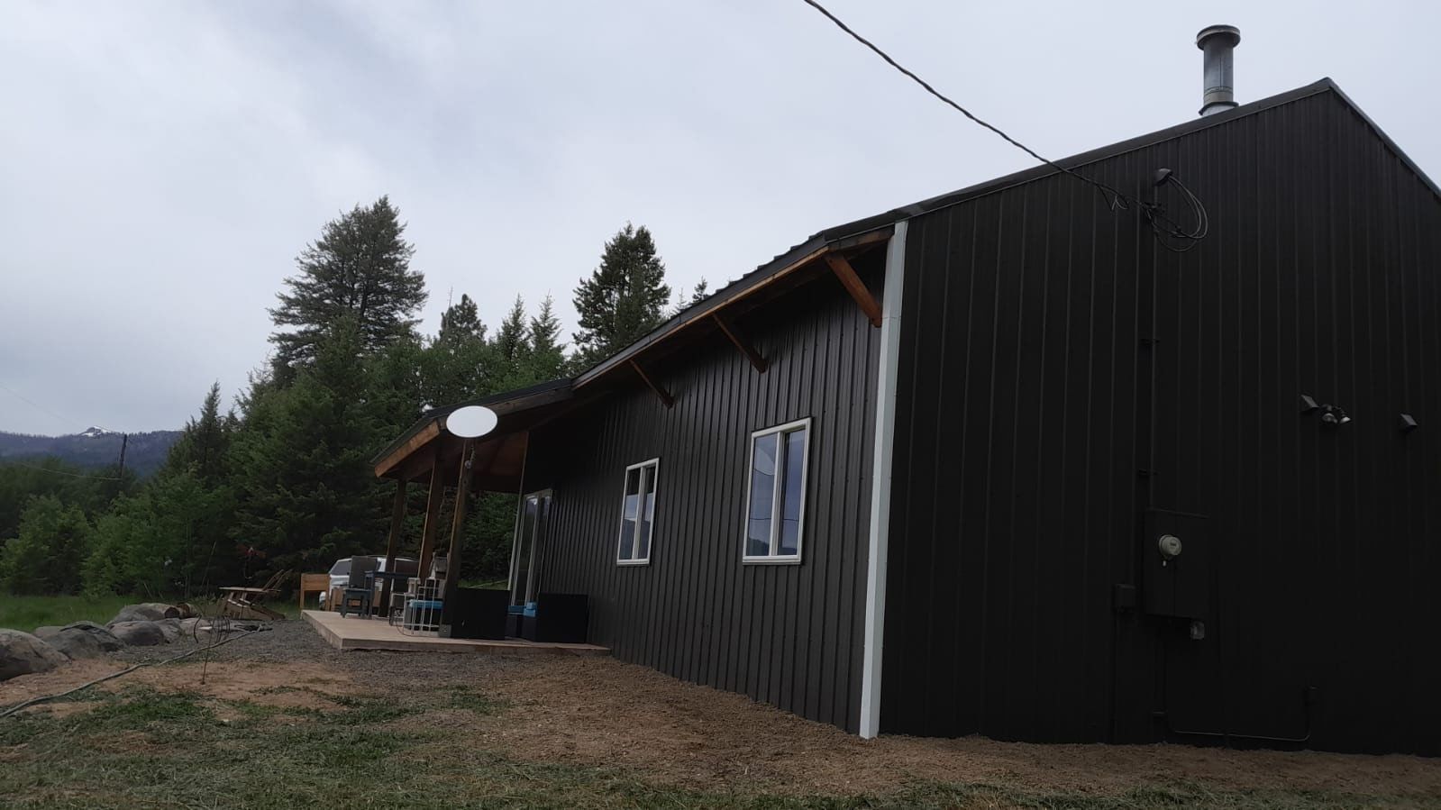 Dark wooden cabin with a sloped roof in a wooded rural area under an overcast sky