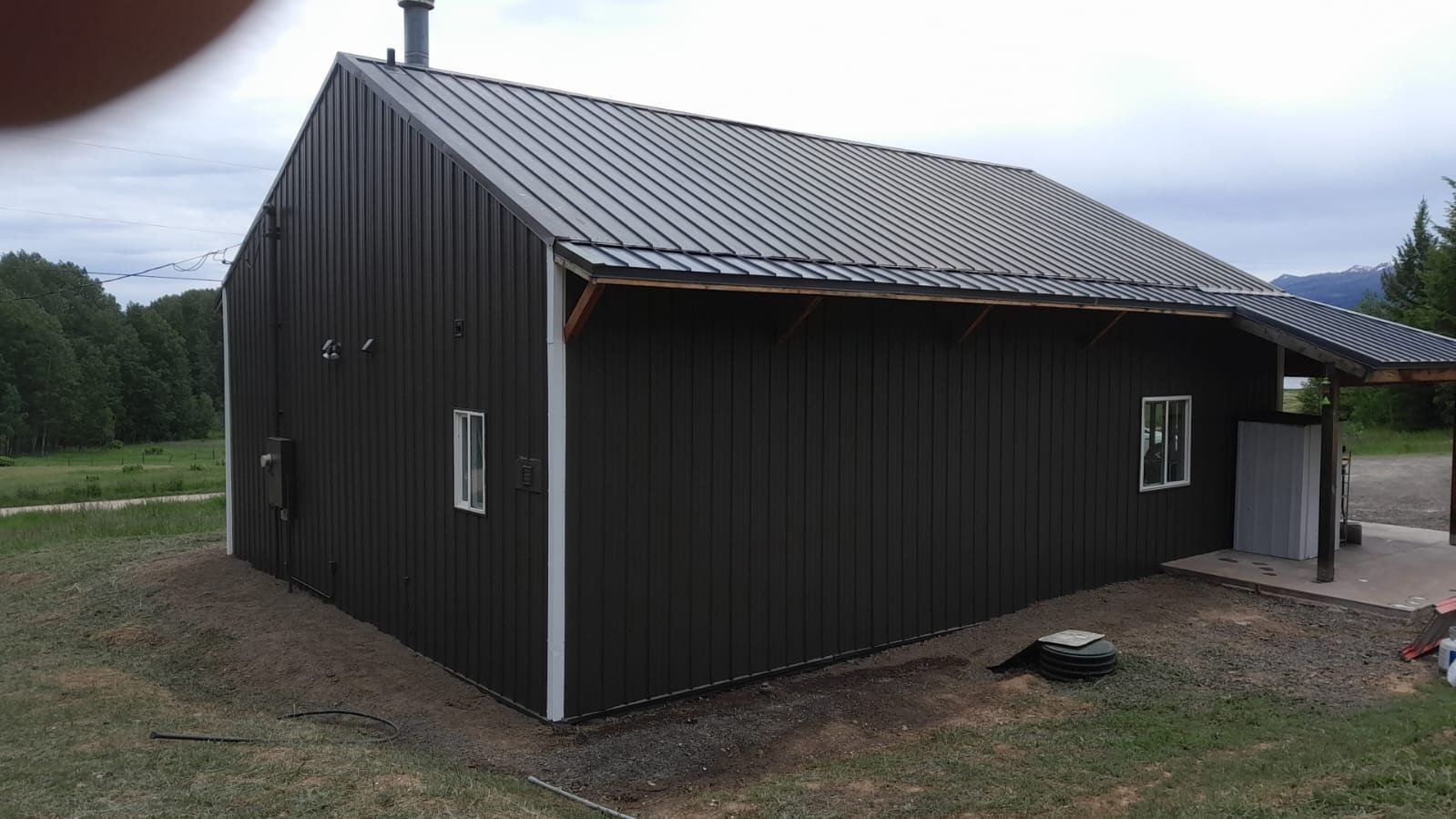 Dark barn-style house with black siding and a gray roof on a rural lot
