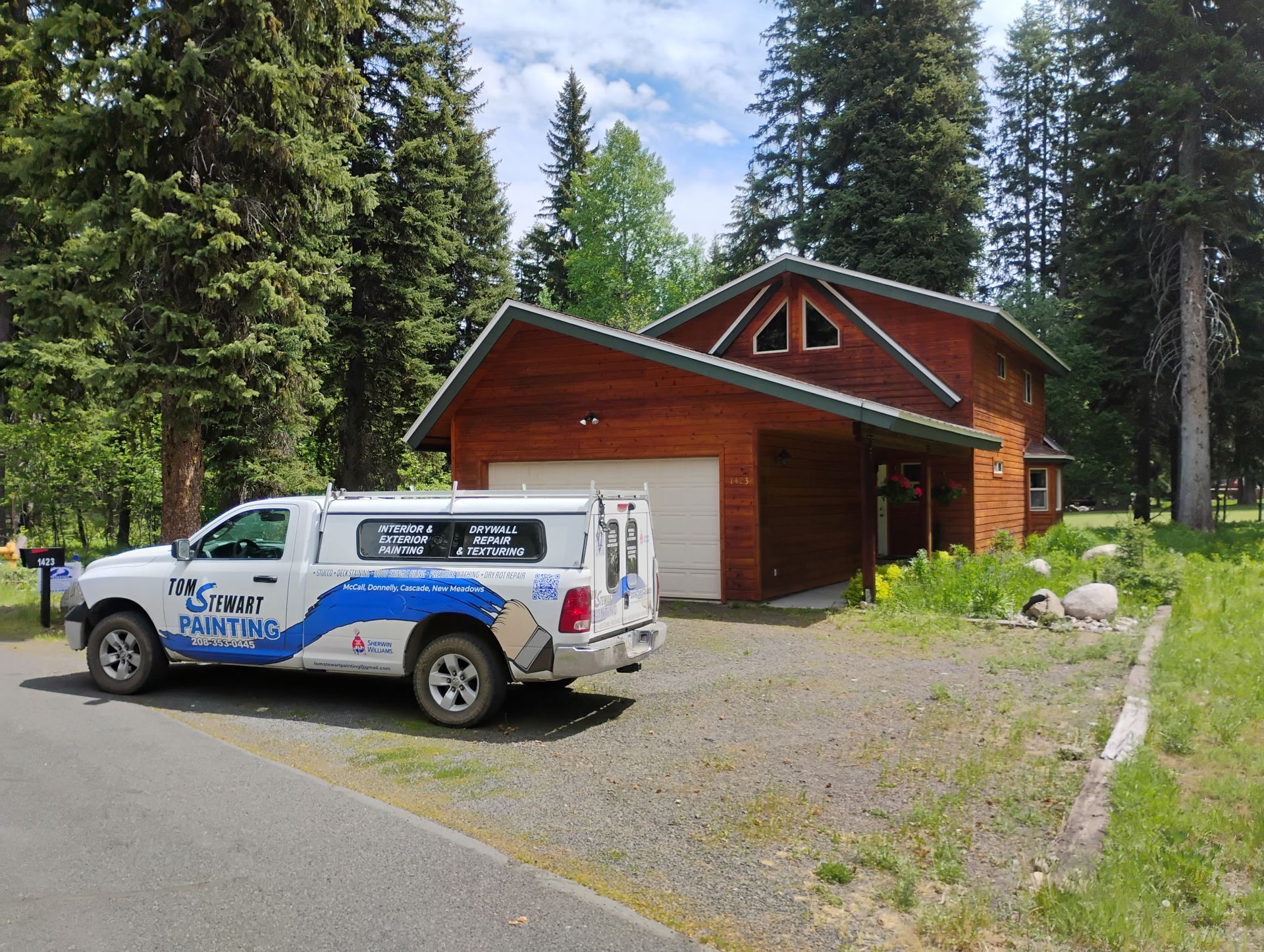 White utility truck parked beside a red cabin in a wooded gravel clearing.