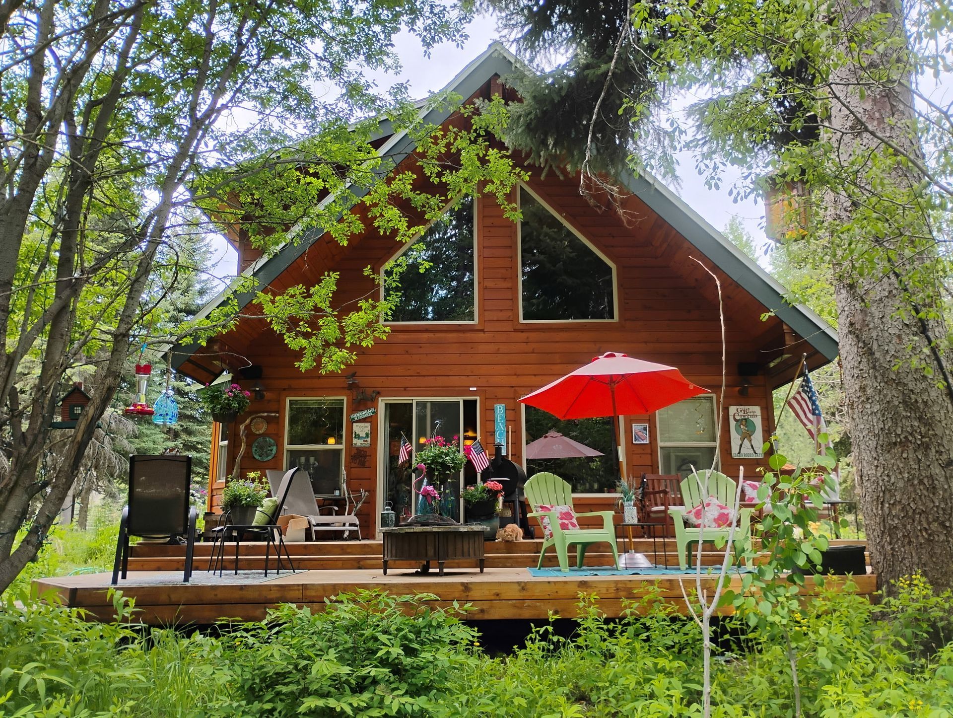 Wooden cabin deck with people gathered under a red umbrella in a lush forest setting