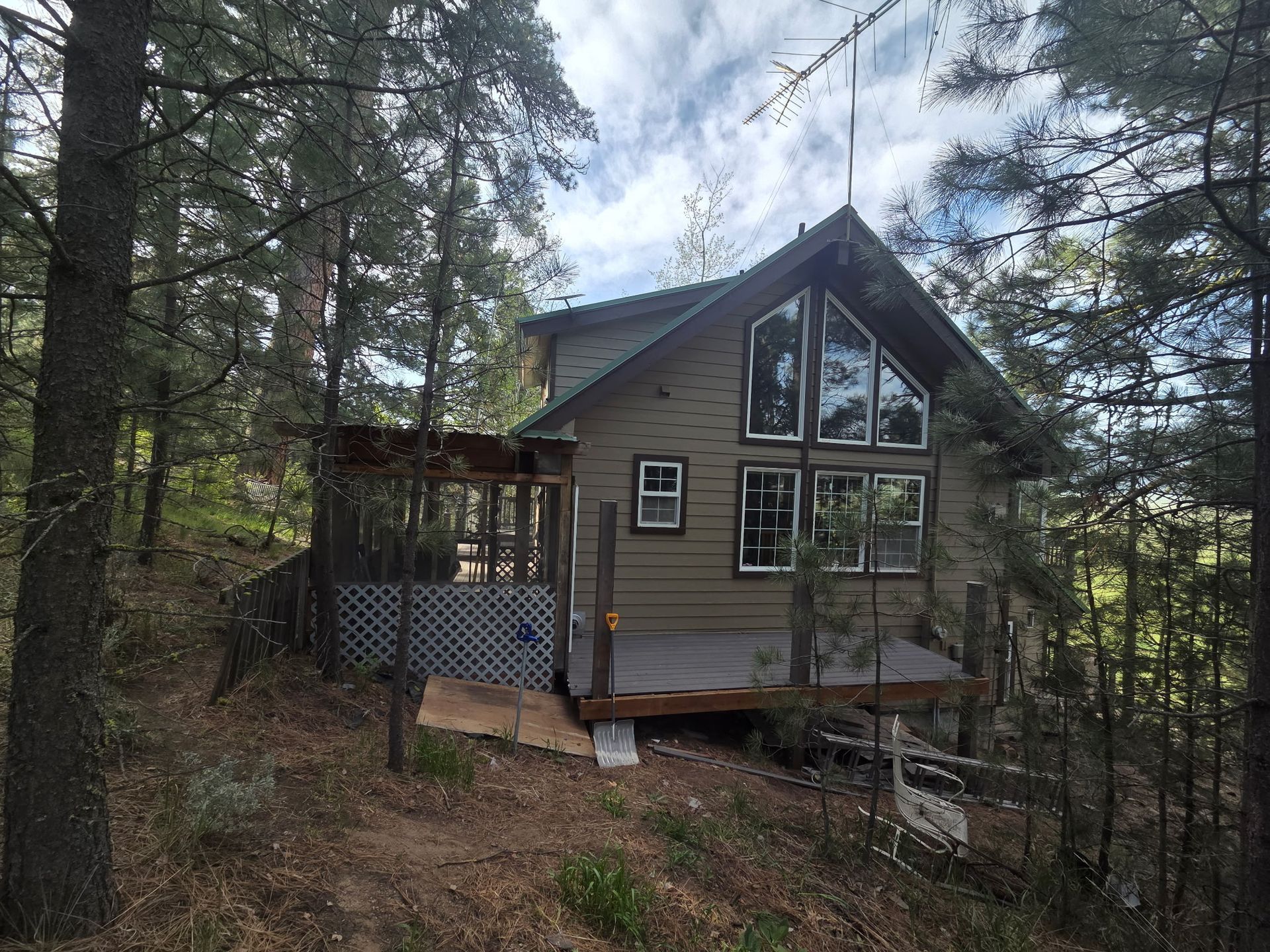 A small gray cabin with a steep roof and porch, nestled among tall pine trees on a wooded slope.