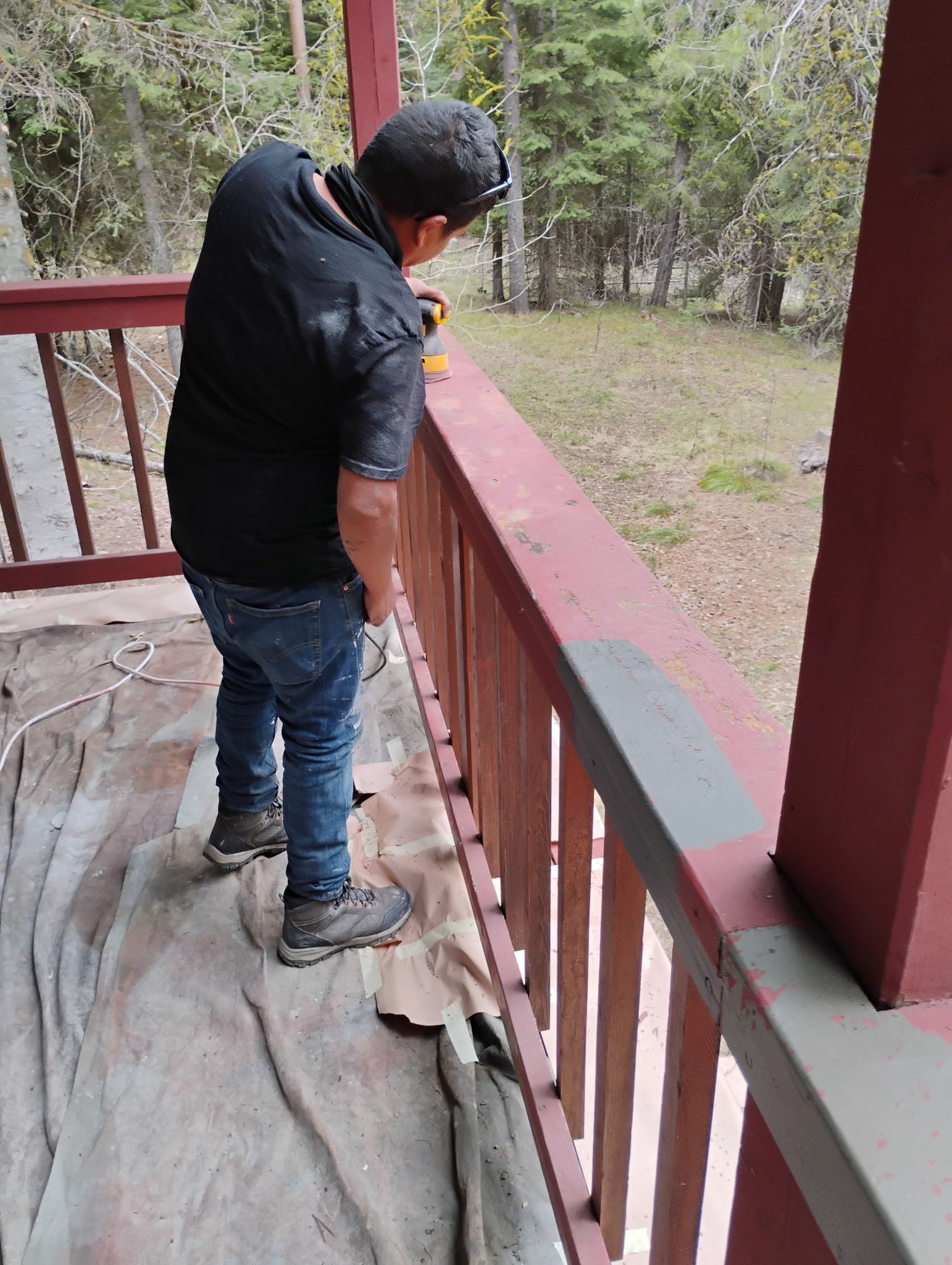 Person standing on a wooden porch, looking over the railing into a wooded area.