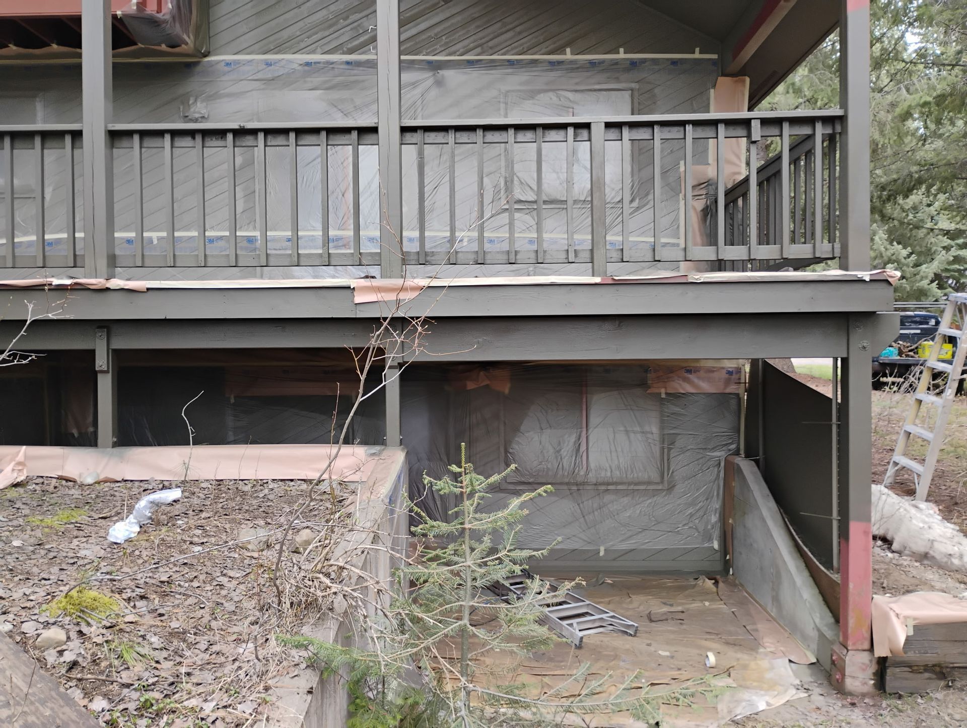 Under-deck storage area with weathered wooden railing, concrete walls, and scattered debris.