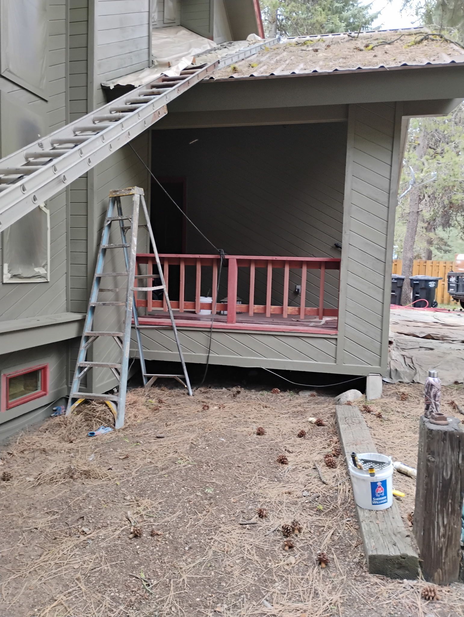 Ladder on roof beside a damaged porch with red railing and debris on the ground