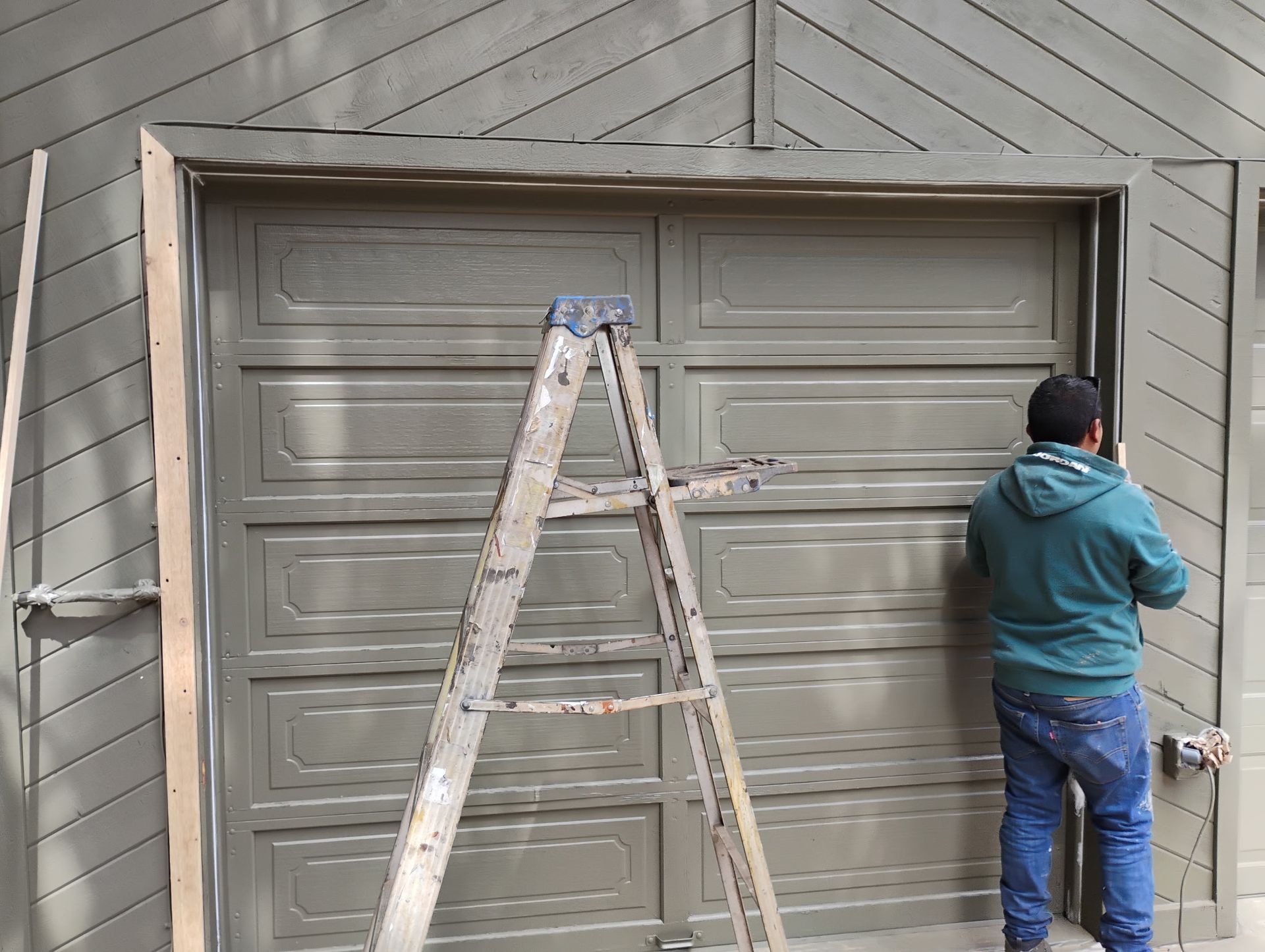 Person painting a garage door beside a ladder and drop cloths