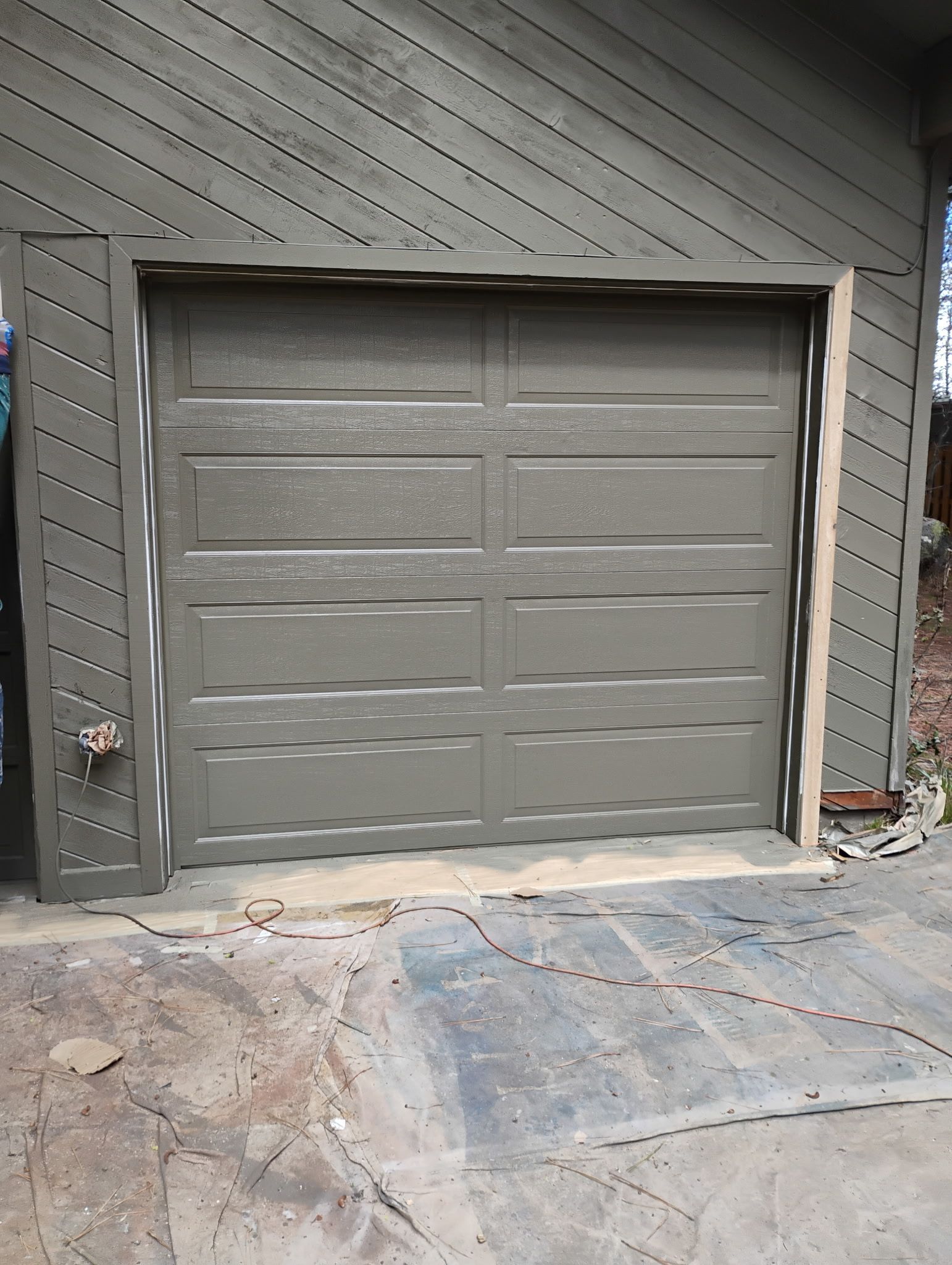 Gray garage door with side vents set in a concrete driveway and siding wall