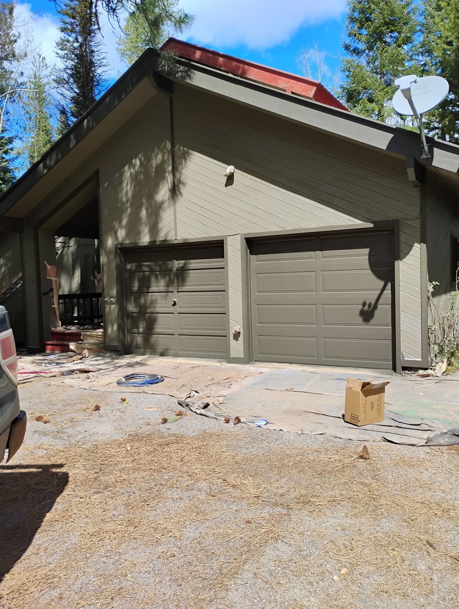 Exterior of a beige garage with two doors, red roof, and a gravel driveway in a wooded area