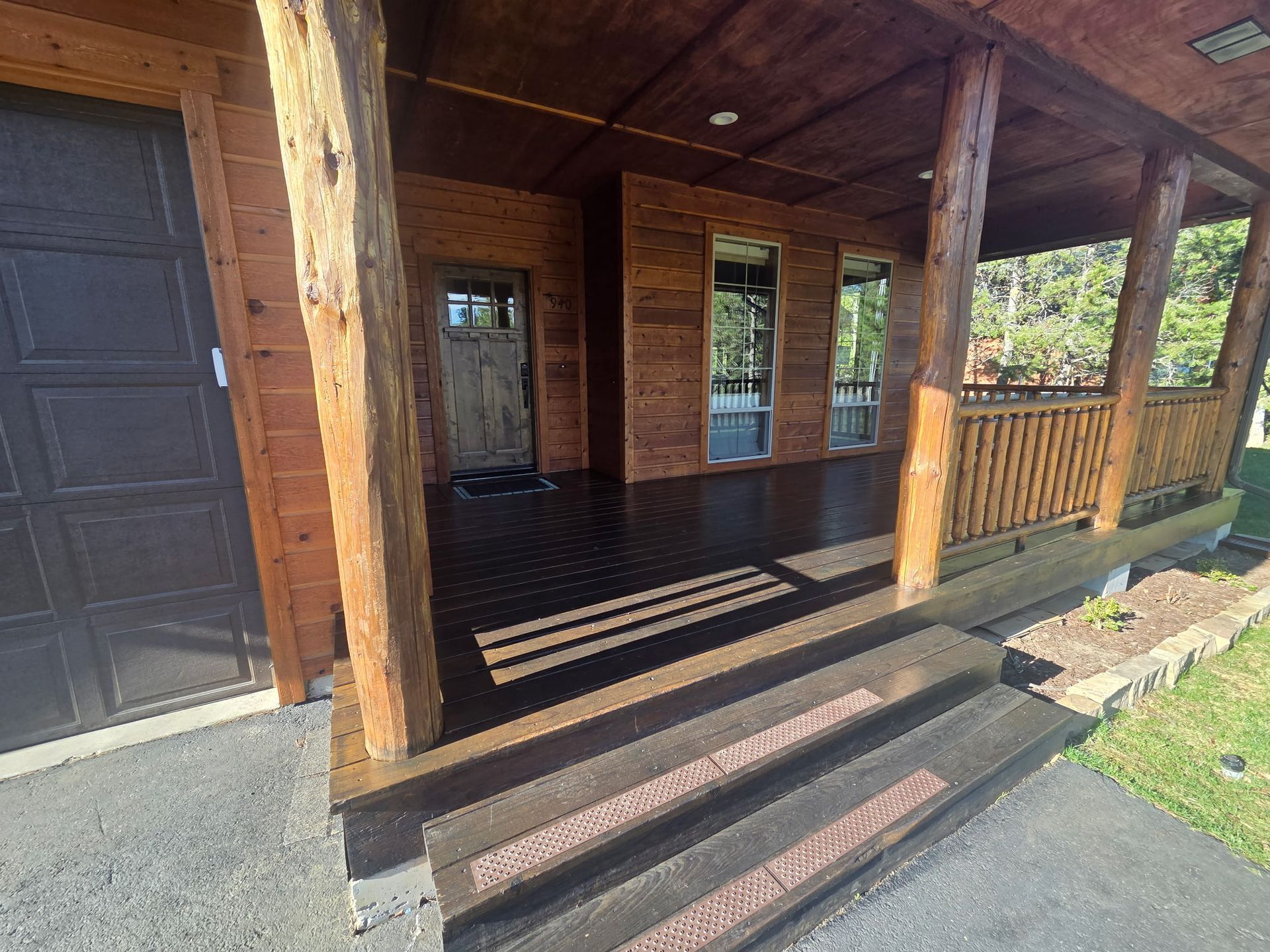 Wooden front porch with steps, railing, and a dark door on a log cabin-style house.