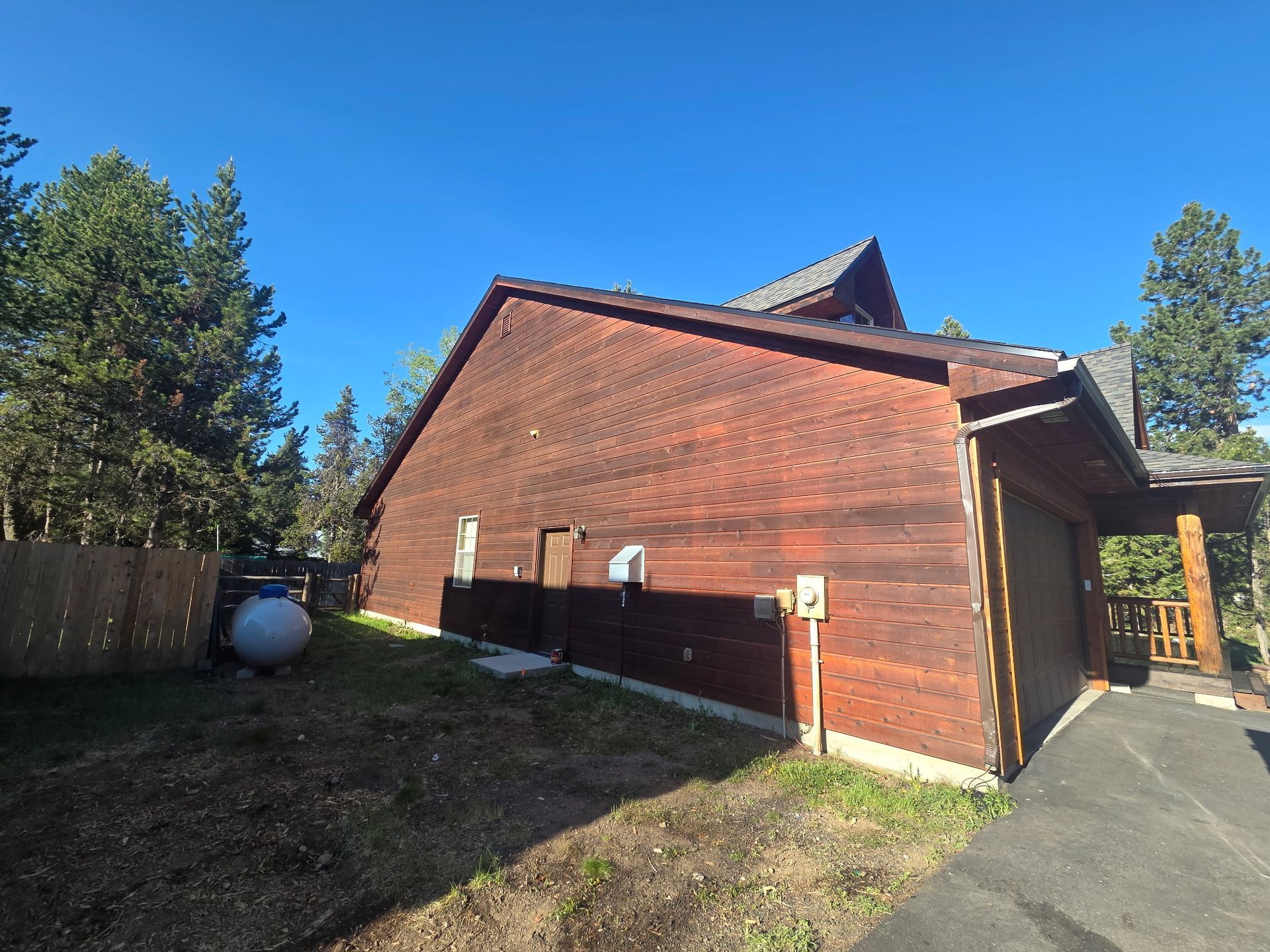 Red brick house with dark roof beside a driveway, under a clear blue sky.