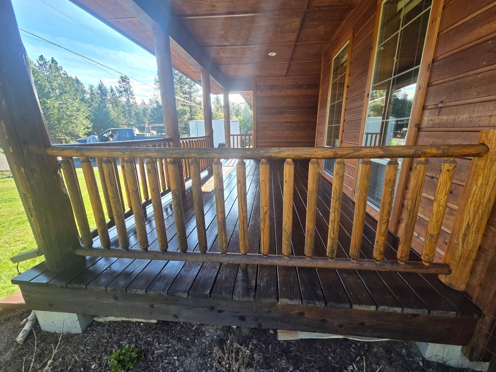 Wooden porch with railing and bench on a cabin, overlooking a sunny green landscape