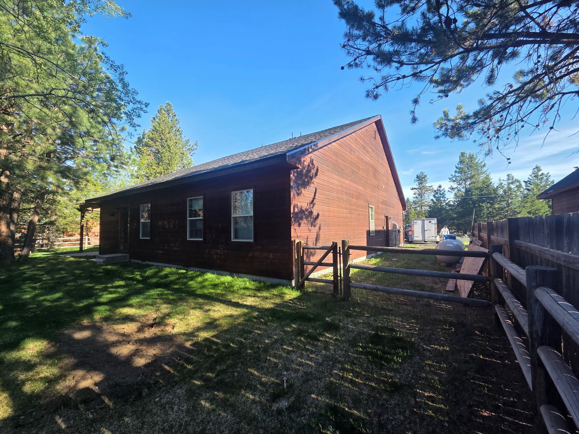 Small brick house with a fenced yard, trees, and a bright blue sky.