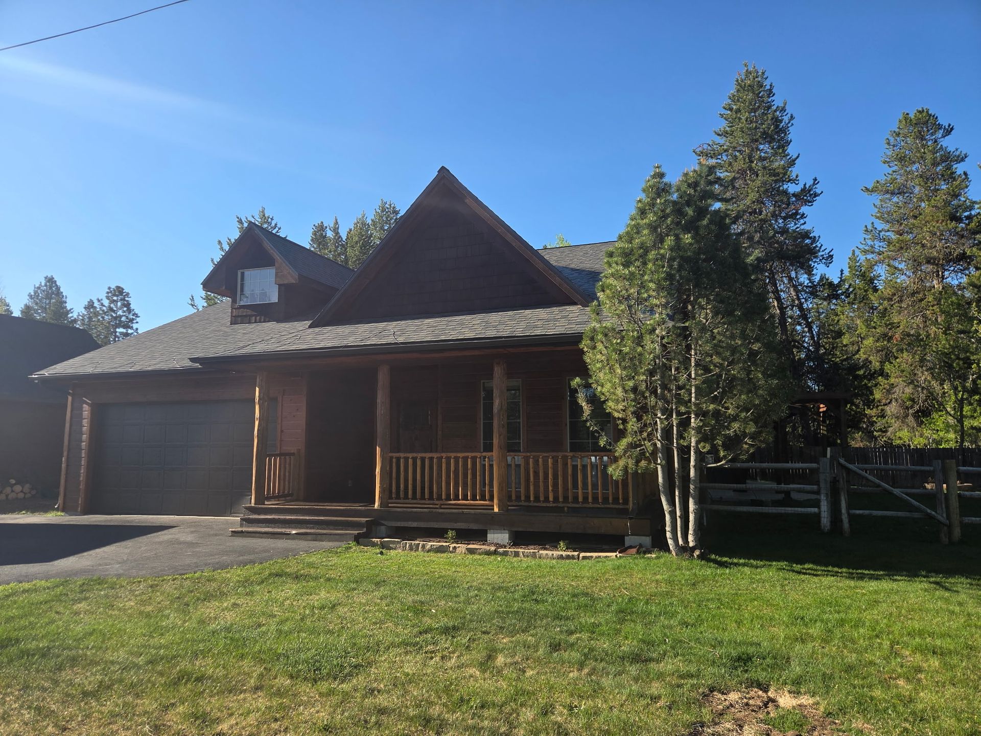 Log cabin-style house with a porch, garage, and green lawn under a clear blue sky