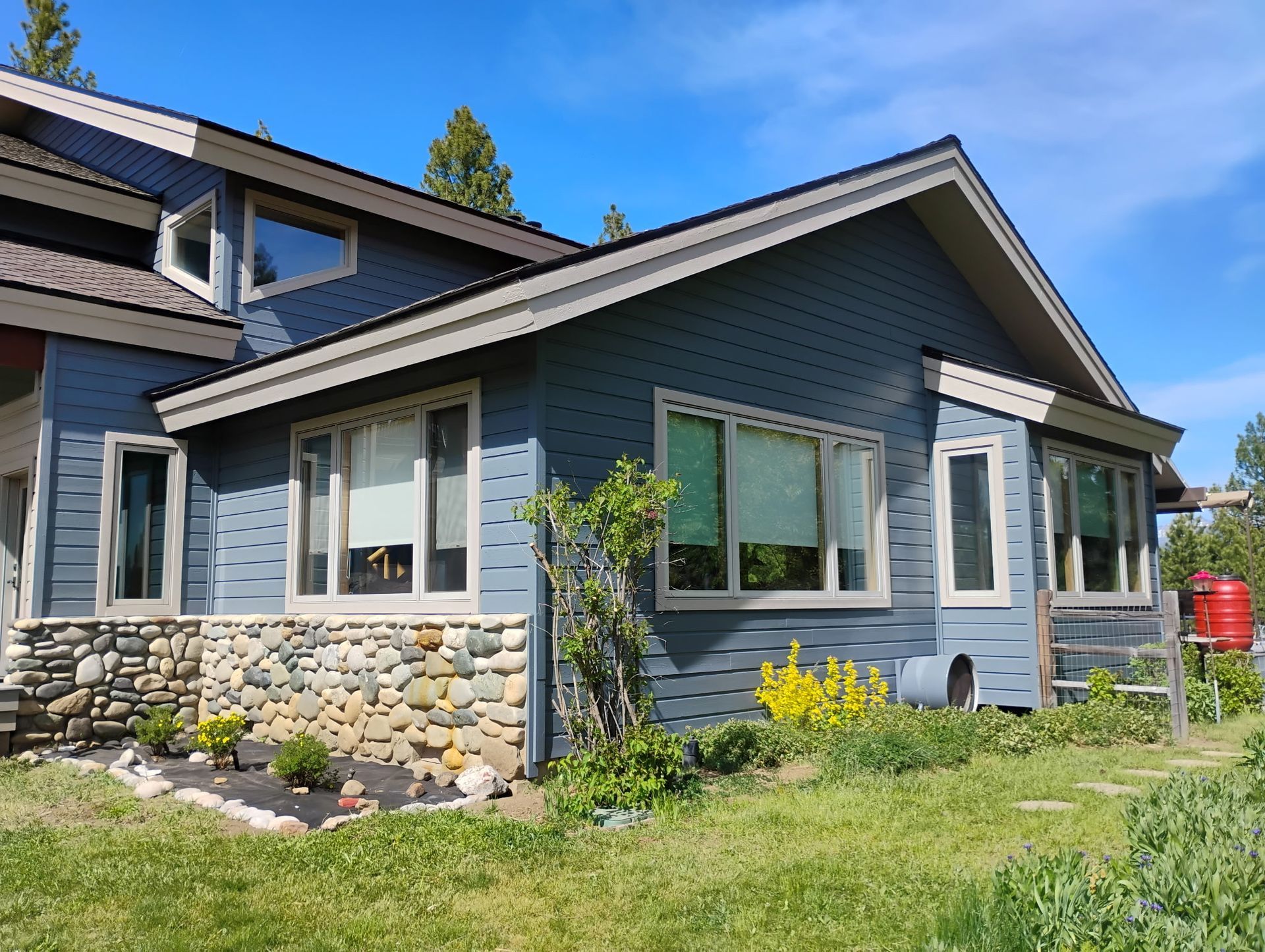 Blue house with stone foundation, white trim, and a grassy yard under a sunny sky
