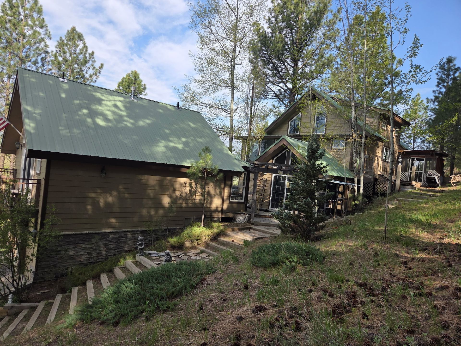 Wooden cabins with green roofs on a wooded hillside under a bright blue sky