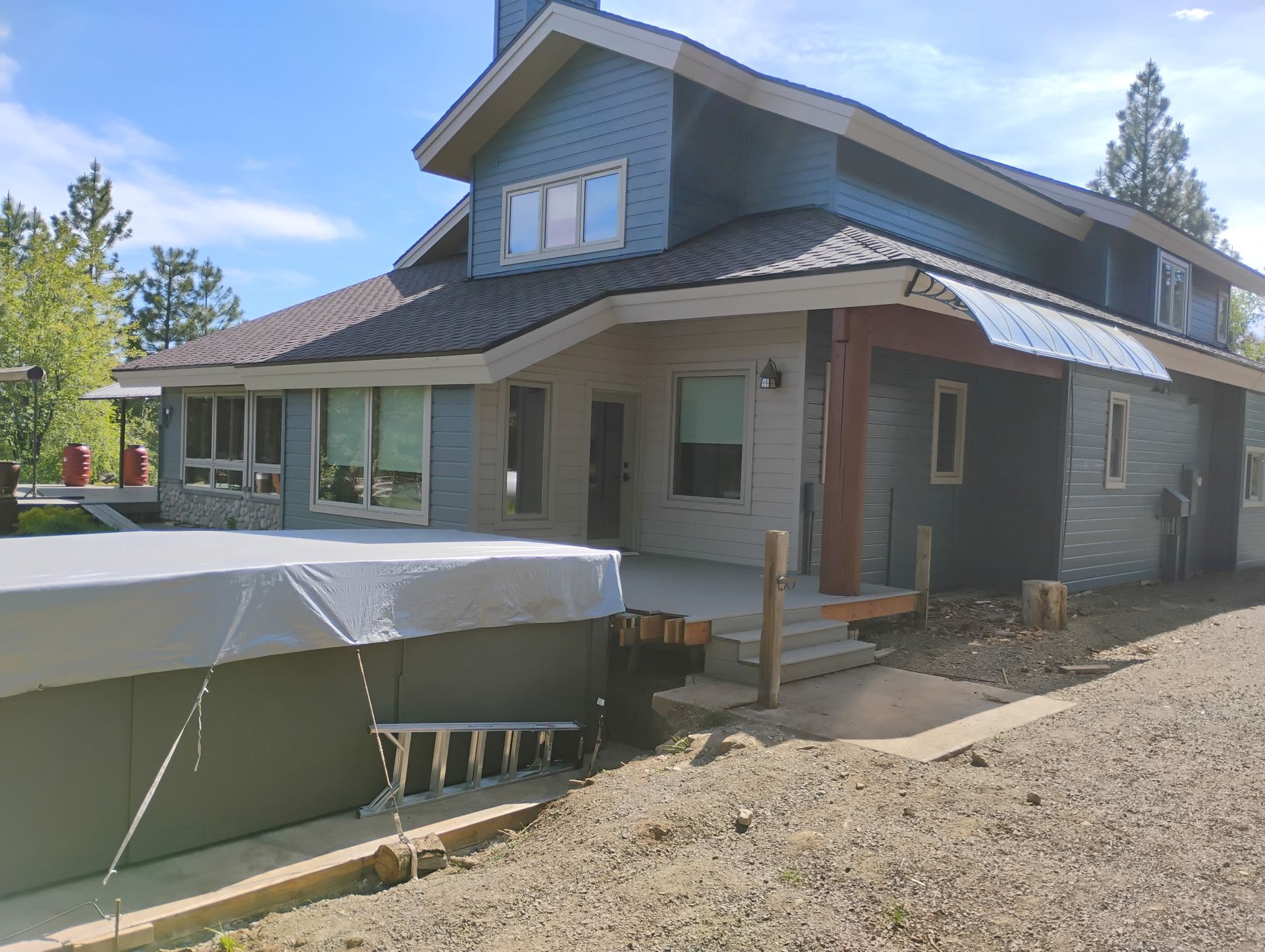 Partially finished house exterior with gravel yard, covered porch, and a large covered object in front