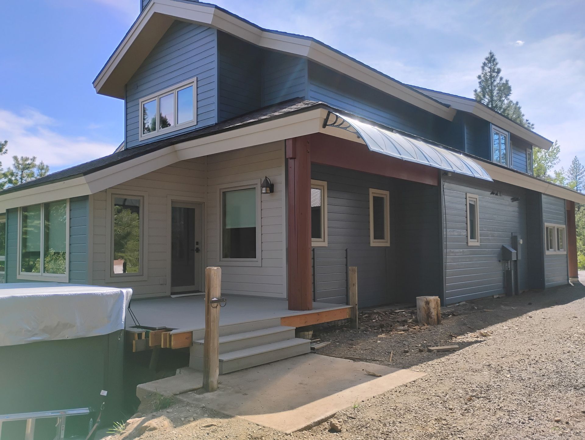 Modern gray two-story house with a front porch and gravel driveway under a clear sky