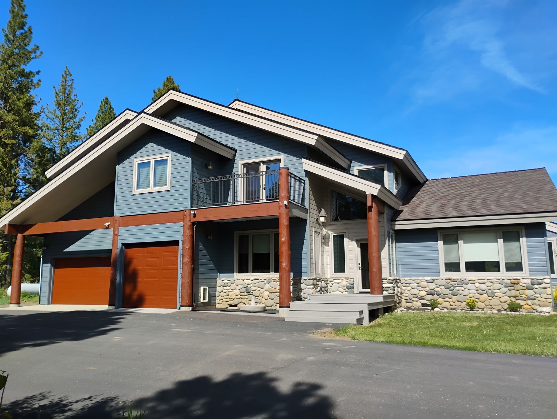 Large modern house with stone and wood accents, two garage doors, and a blue sky backdrop