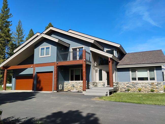 Large modern house with gray siding, stone accents, and red garage doors under a blue sky