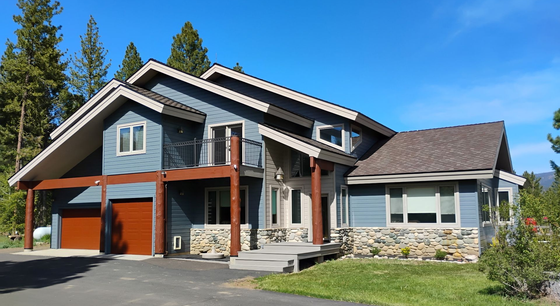 Modern two-story house with stone and wood exterior, large garage, and landscaped front yard under blue sky