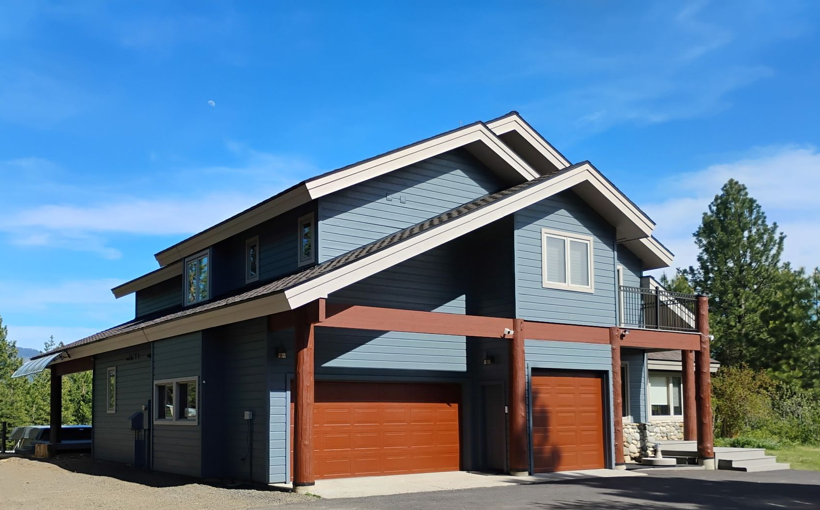 Modern two-story house with gray siding, wood accents, and two orange garage doors under a blue sky