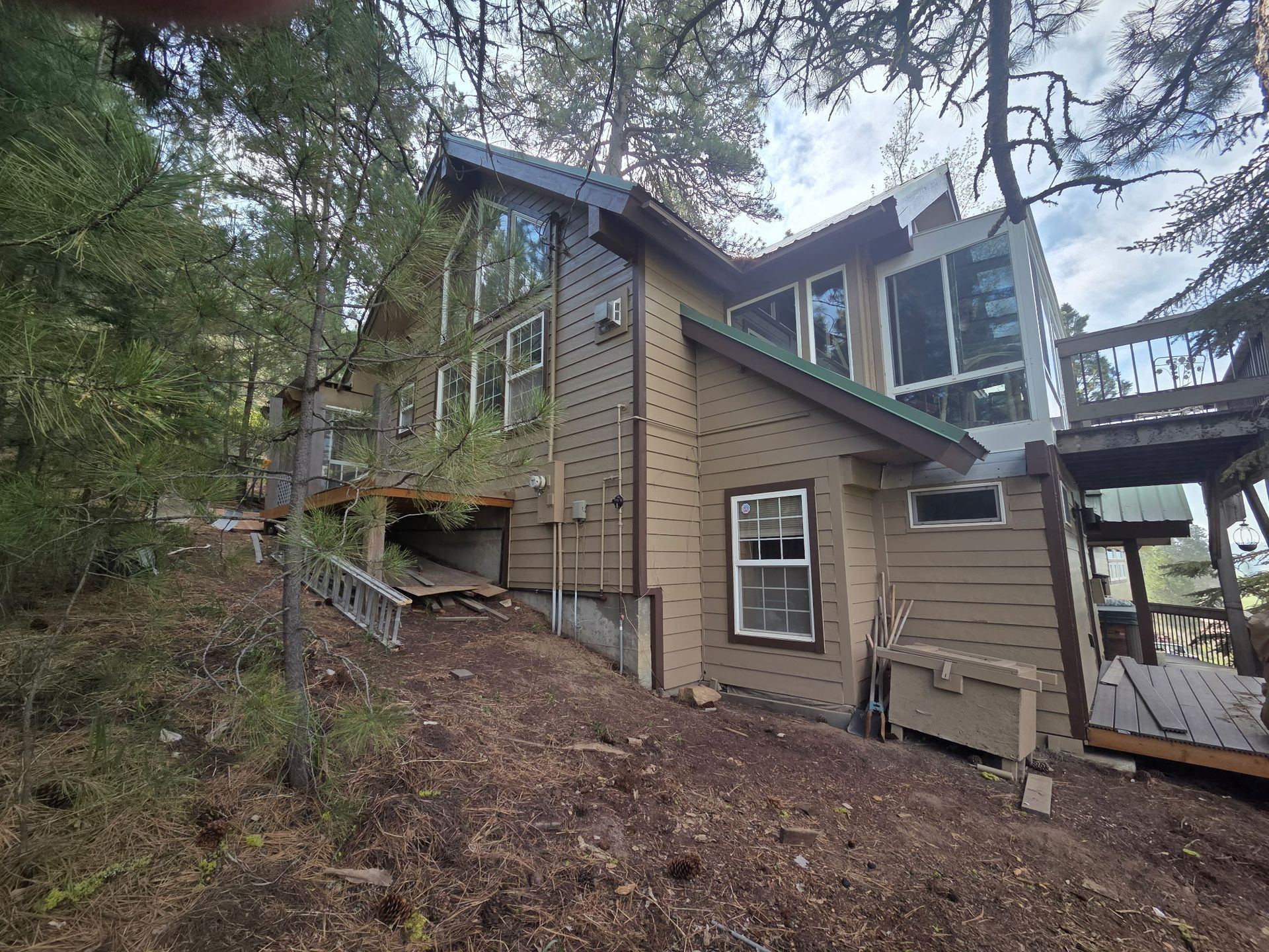 Wooded hillside house exterior with tan siding, large windows, and a sloped roof