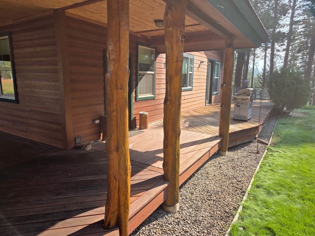 Wooden cabin porch with log posts, deck steps, and a green lawn beside it