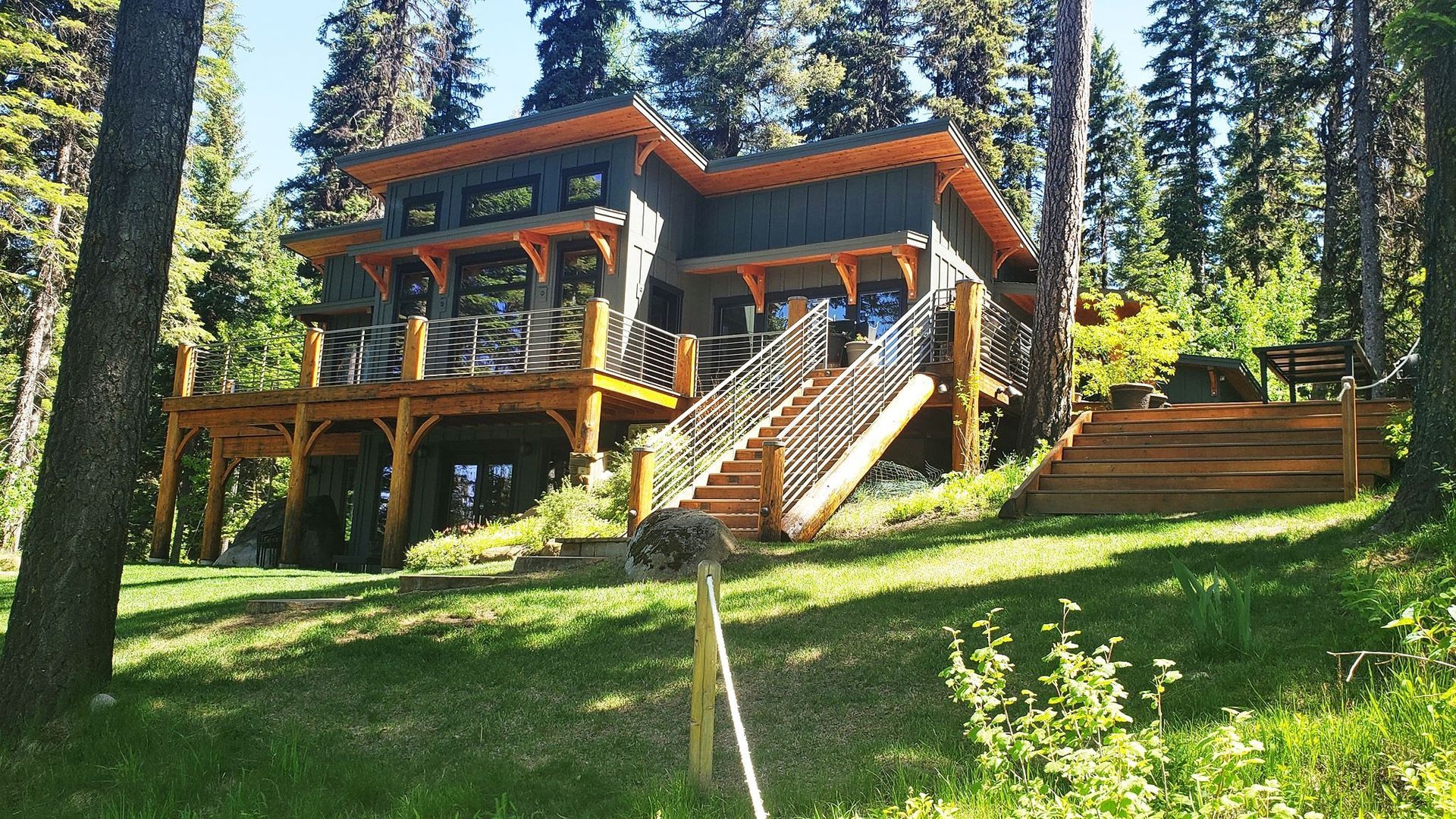 Wooden cabin on a sunny forest hillside with tall pine trees and a central staircase