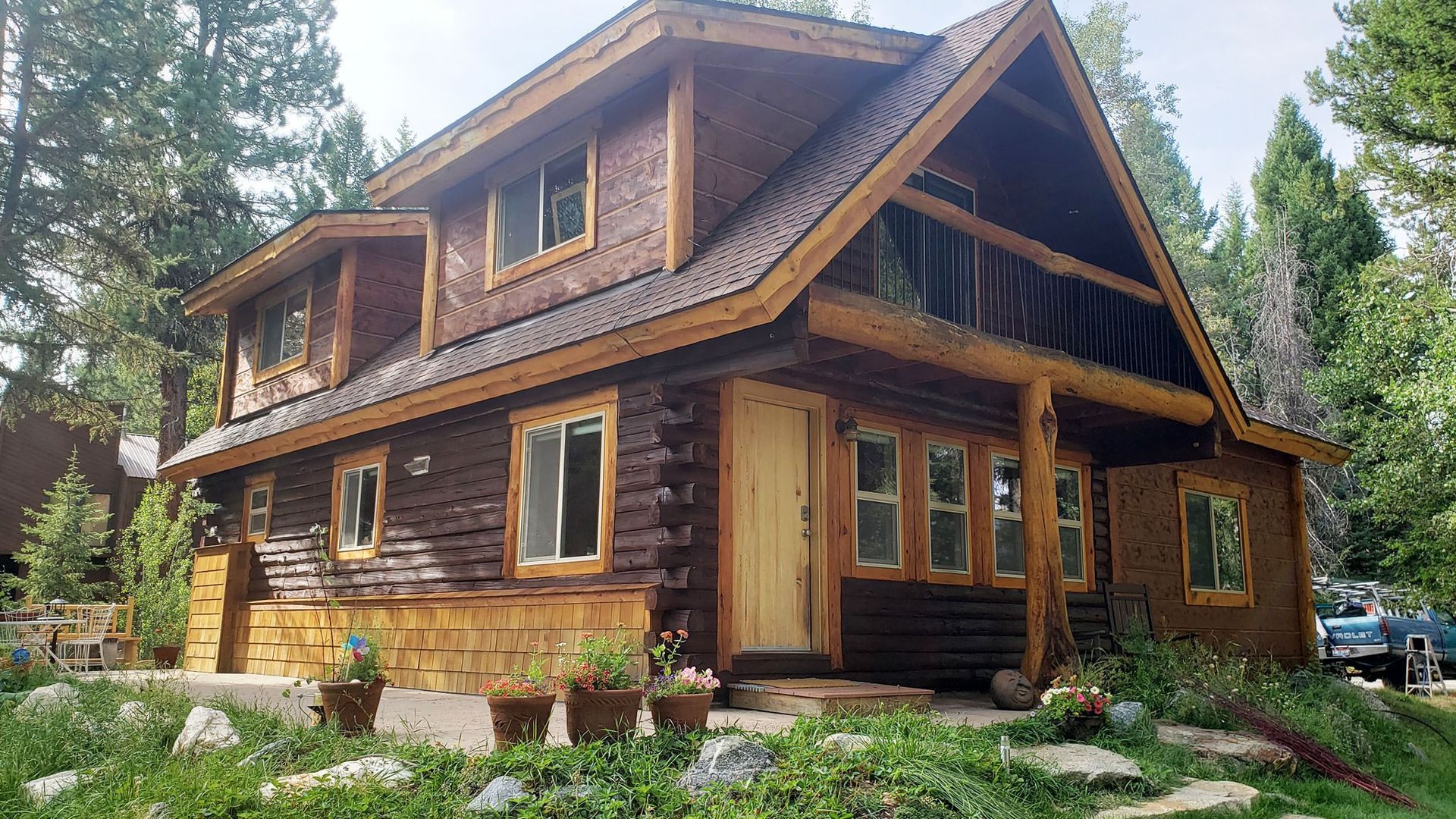 Rustic log cabin with a steep roof and stone foundation in a wooded garden setting