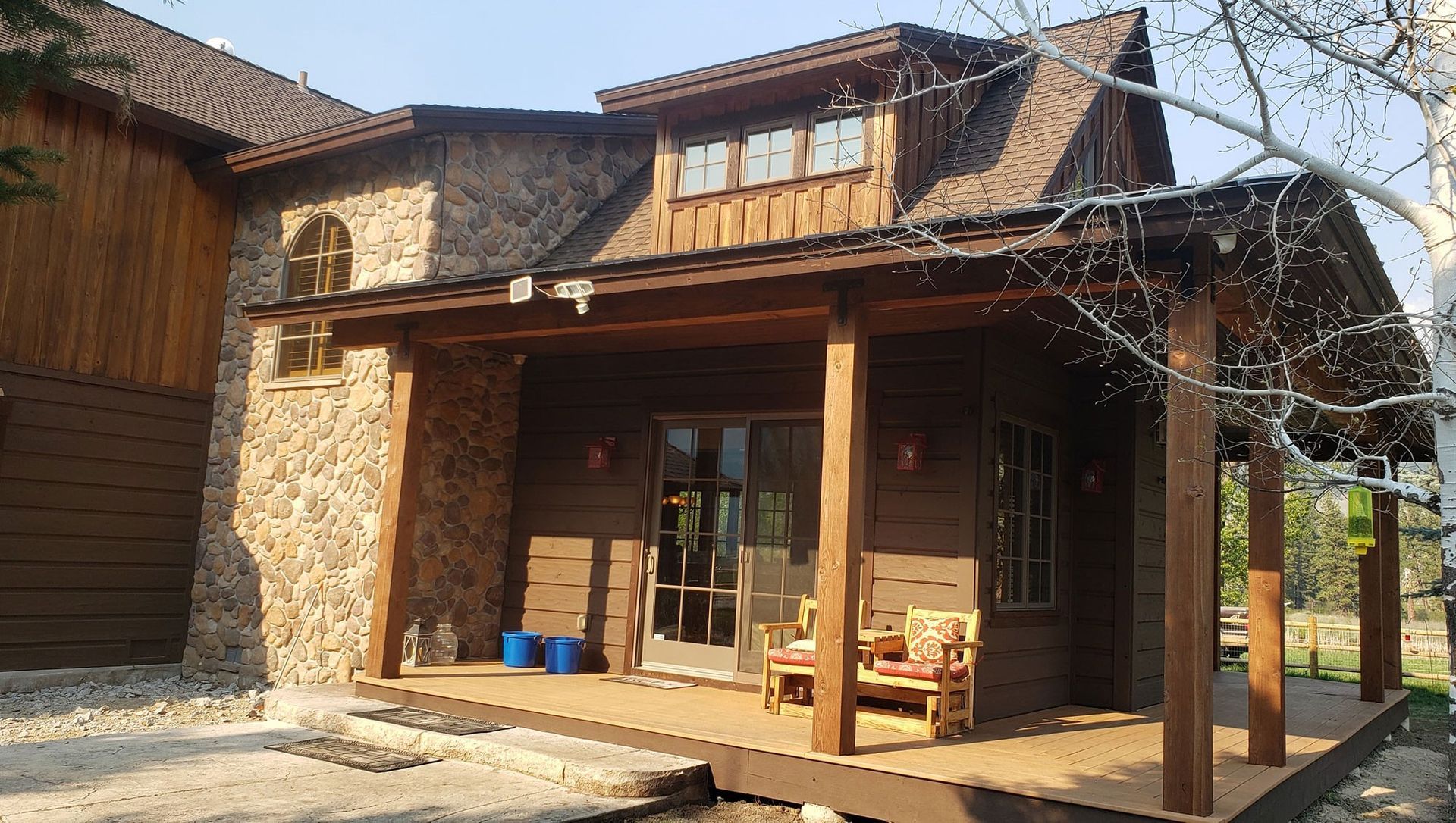 Rustic stone house entrance with wooden porch, glass door, and blue buckets in front