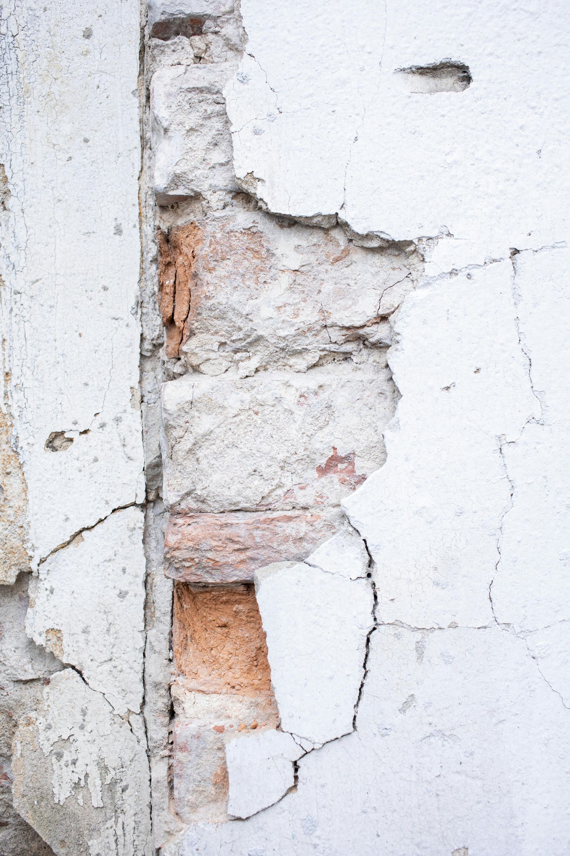 Cracked white wall with chipped plaster exposing red brick underneath
