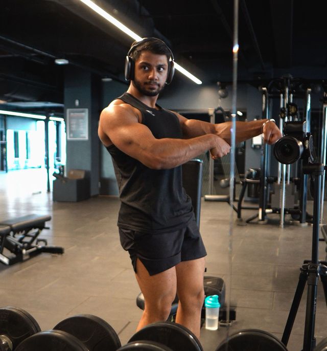 Kamal wearing headphones is lifting a dumbbell in a gym