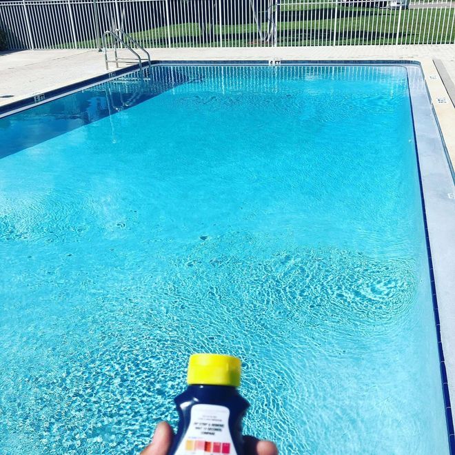 Bottle of sunscreen held by a pool with blue water and a diving board in the background