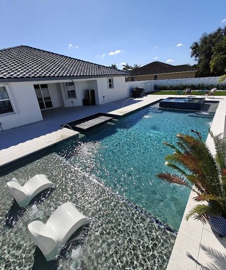 Modern backyard pool with blue water, white lounge chairs, and a white house under a clear sky