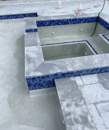 Partially tiled swimming pool with gray concrete deck and blue mosaic tile edging