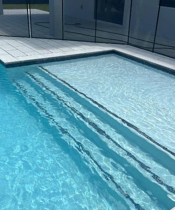 Outdoor swimming pool with clear blue water and shallow steps beside a tiled deck