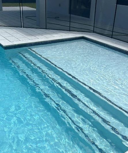 Outdoor swimming pool with clear blue water and shallow steps beside a tiled deck