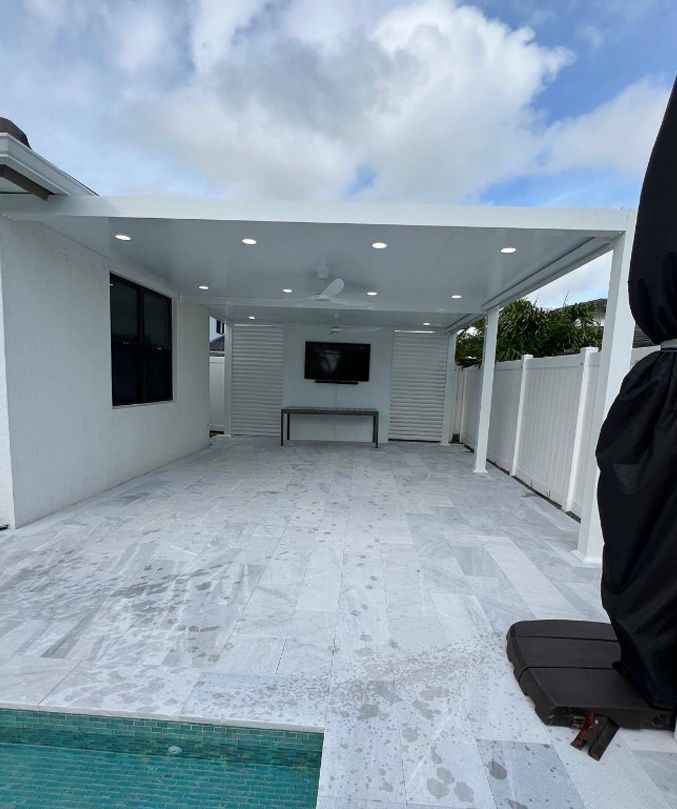 Modern white patio with tiled floor, covered seating area, and outdoor TV under a bright sky