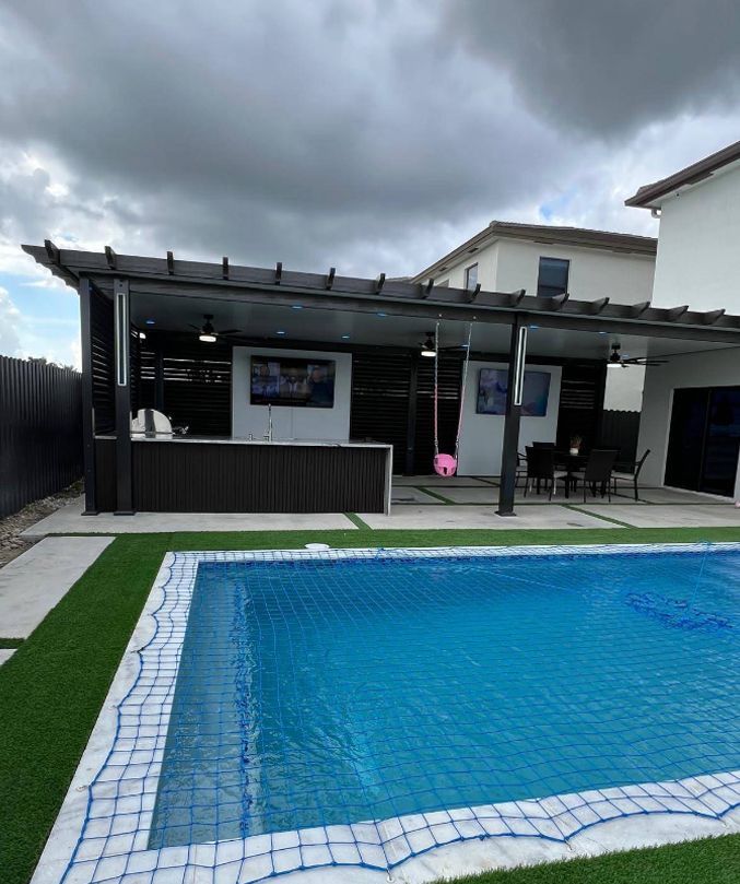 Backyard pool beside a covered patio under cloudy skies