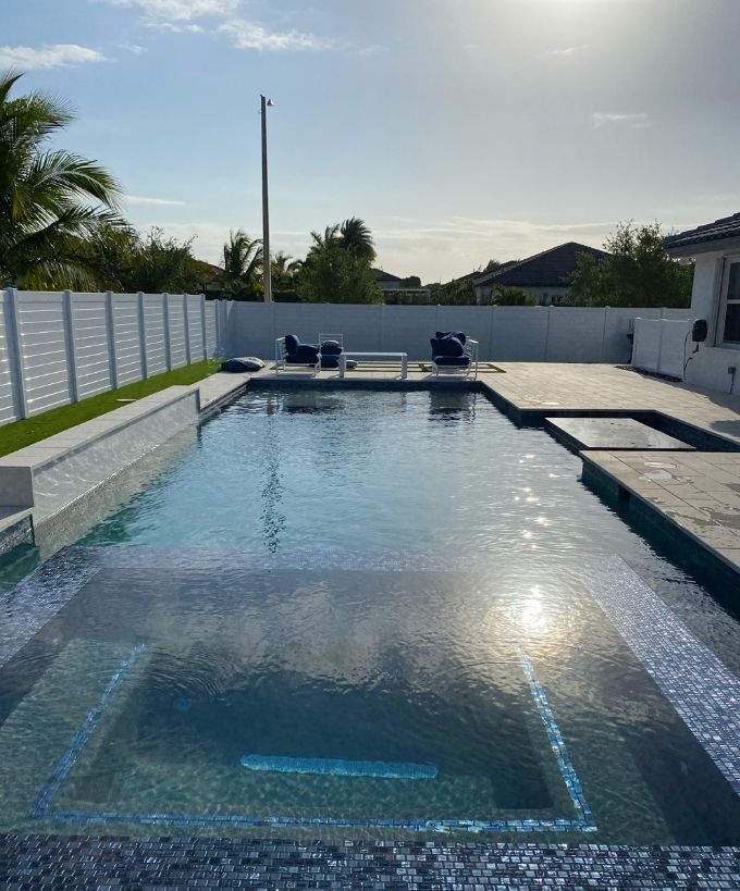Backyard pool with lounge chairs, white fence, and bright sun reflecting on the water